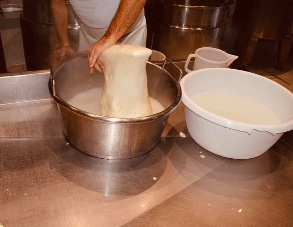 Dans l'atelier, deux mains soulèvent la pâte filée au-dessus de la cuve d'eau chaude, à côté d'une bassine blanche